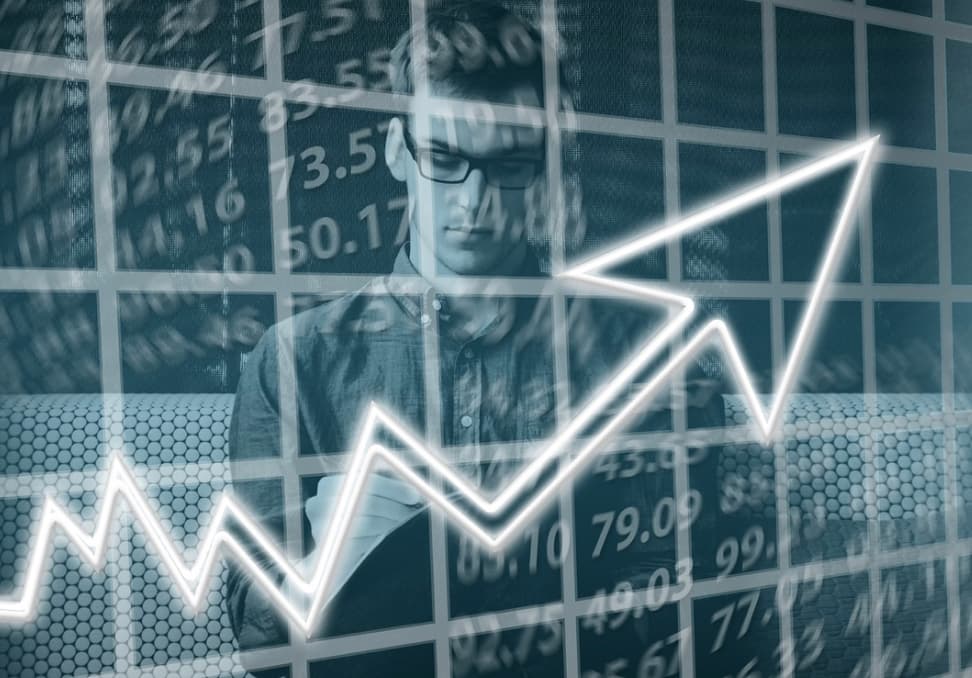 Composite image of a man with glasses superimposed over a background of stock market figures and graphs, with a bright, rising arrow symbolizing growth
