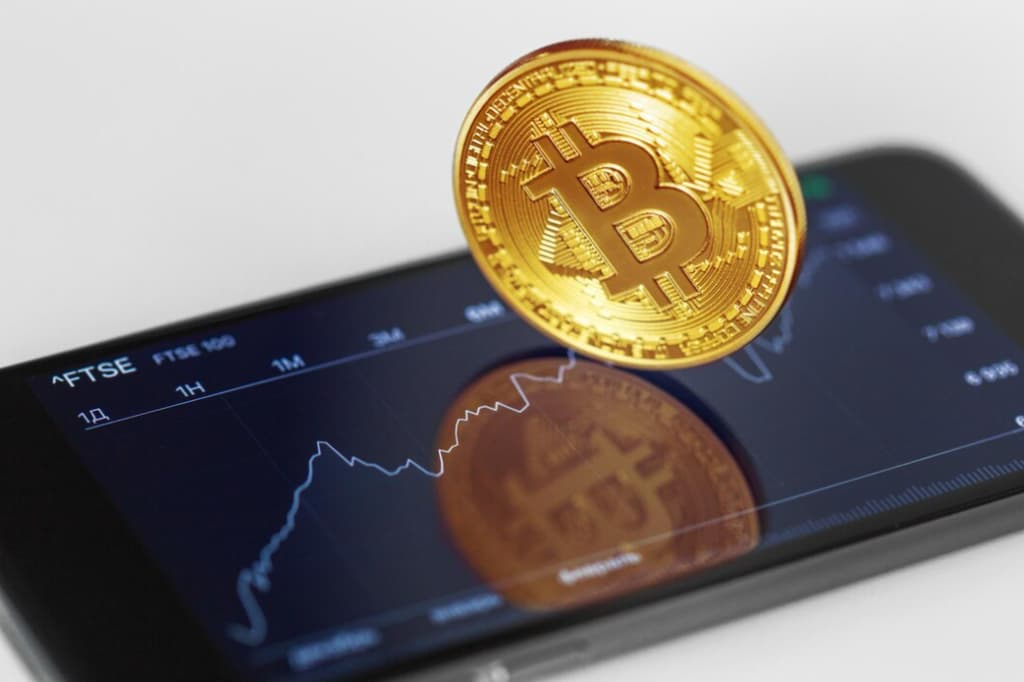 A Bitcoin coin rests on a smartphone displaying market graphs