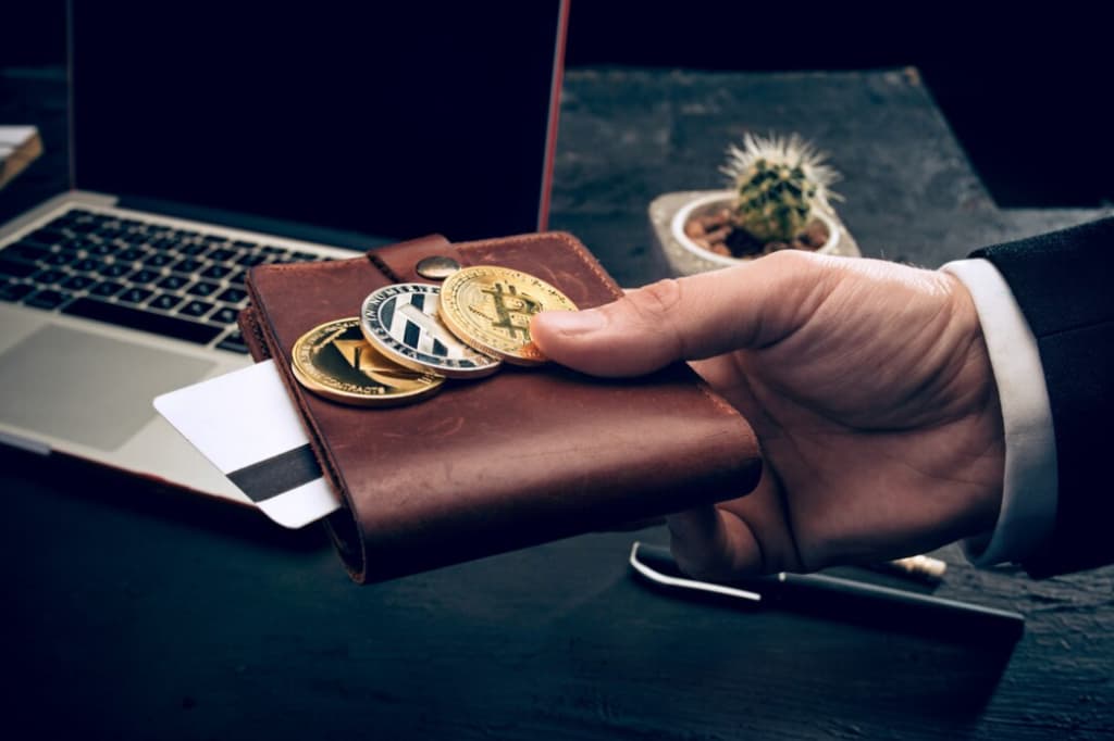 hand holds a wallet with bitcoin on it, a laptop on the table in the background