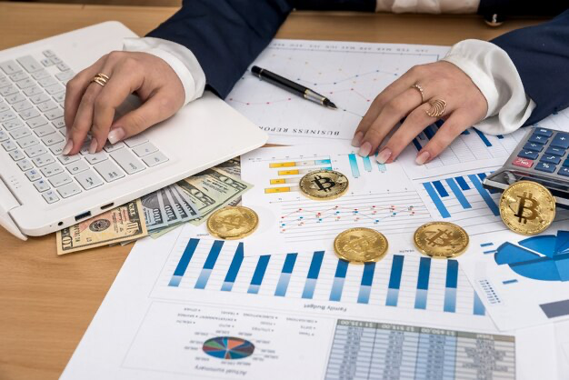 Woman's hands on papers, laptop, bitcoin and dollar next to her